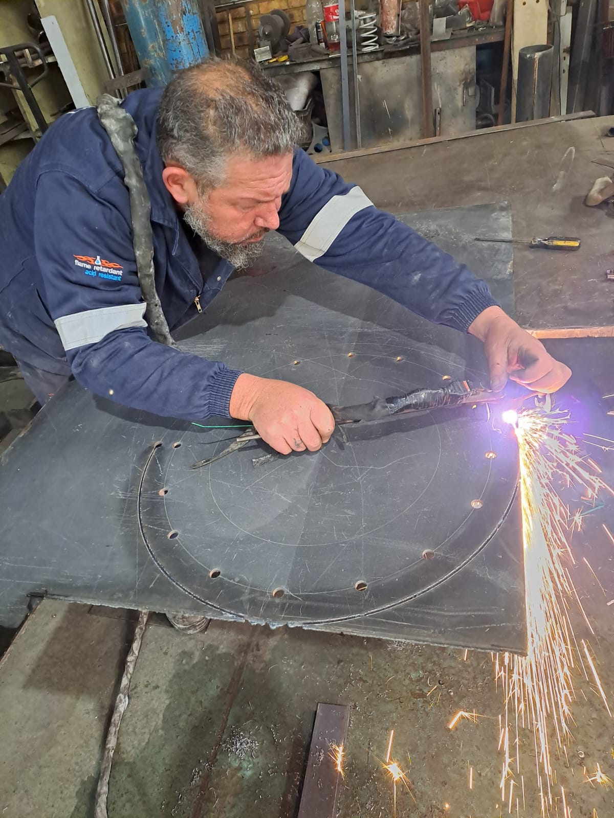 Fabricator cutting circular steel plate with sparks