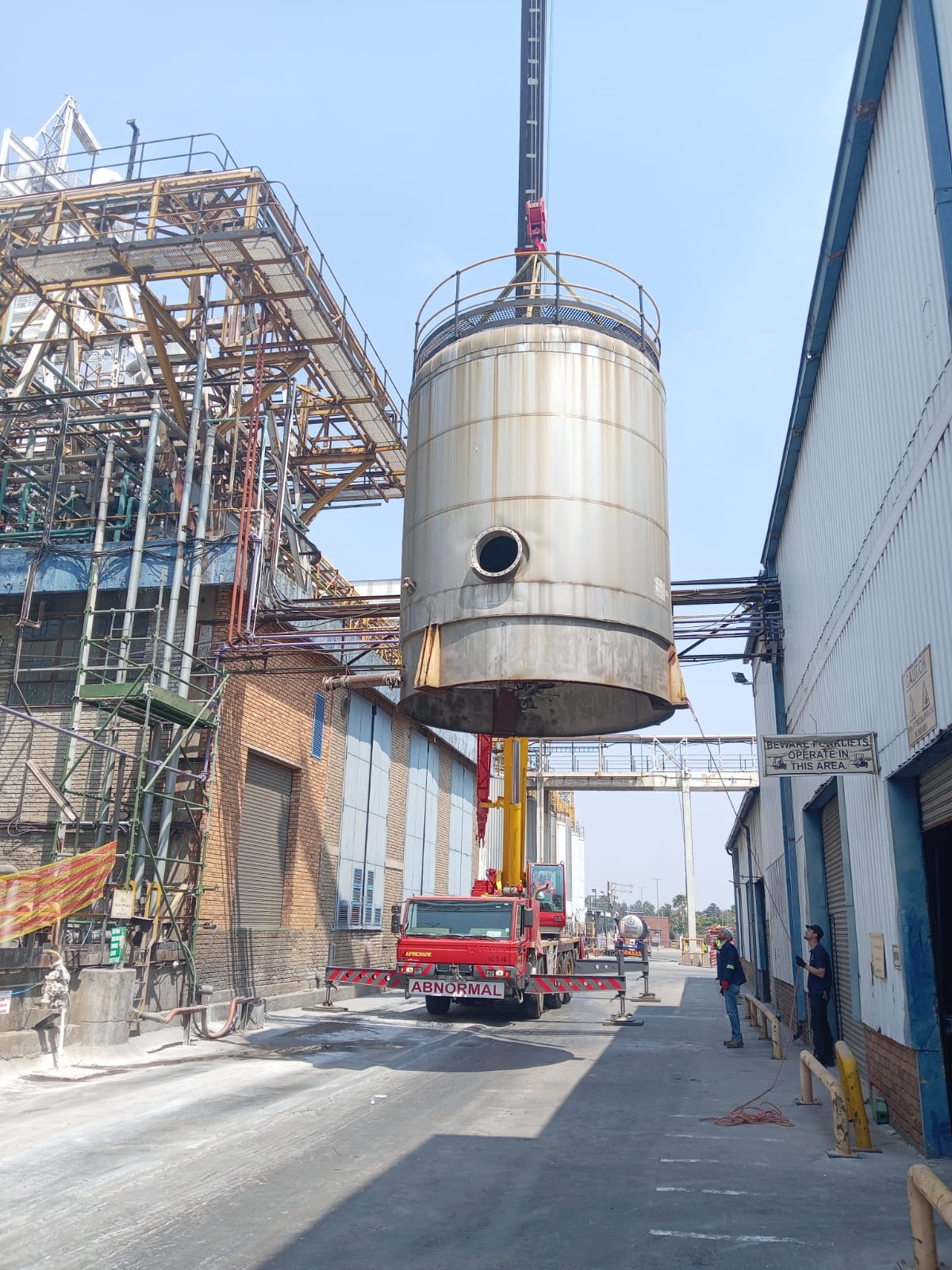 Mobile crane lifting industrial vessel between buildings