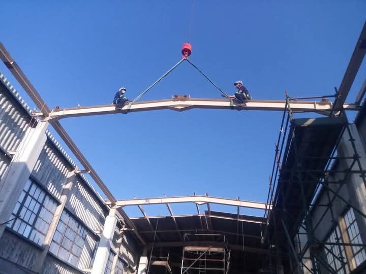 Workers riding a structural steel beam during a lift